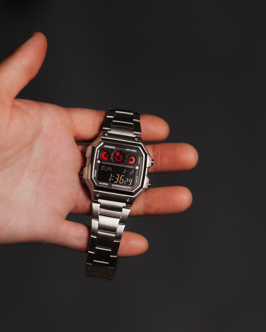 EON Redline Full Metal AE-1300 custom Casio digital watch with red and black display, stainless steel case and bracelet, held in hand.