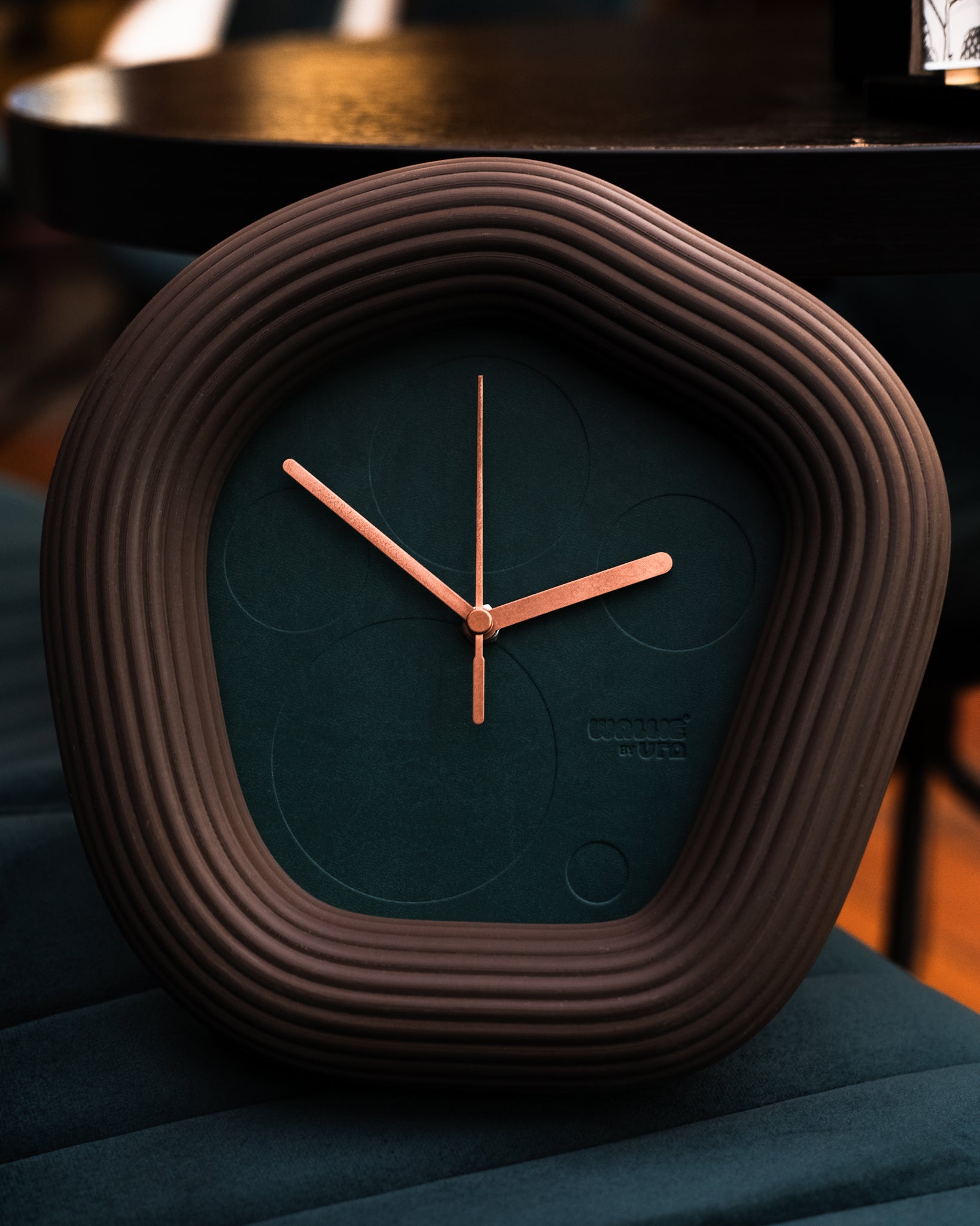 Round Wallie clock with ribbed brown frame and green face on a dark surface made by Ura Watches / EON TIME