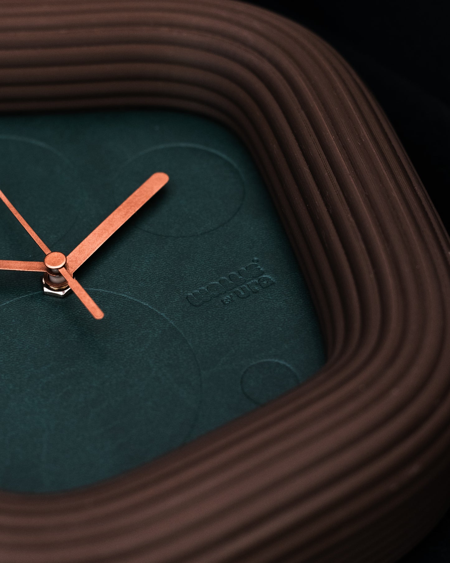 Wallie Clock with brown casing and brss hands on a dark background. Made by Ura Watches / EON TIME