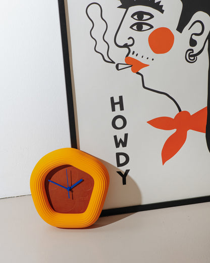 Orange Wallie clock with blue hands in front of a stylized portrait with 'HOWDY' text. made by Ura Watches / EON TIME
