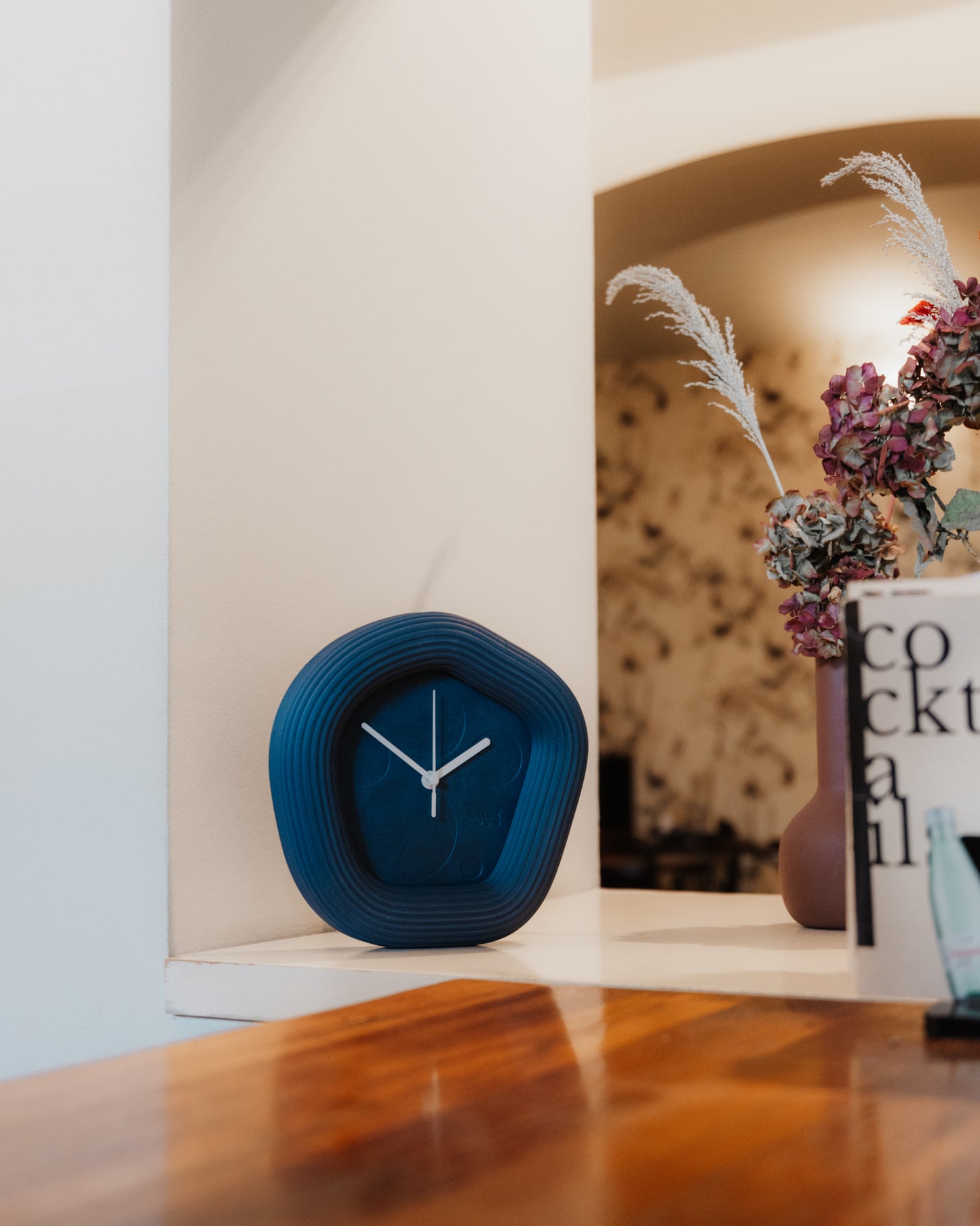 Blue clock on a wooden surface with a blurred background. Made by Ura Watches.