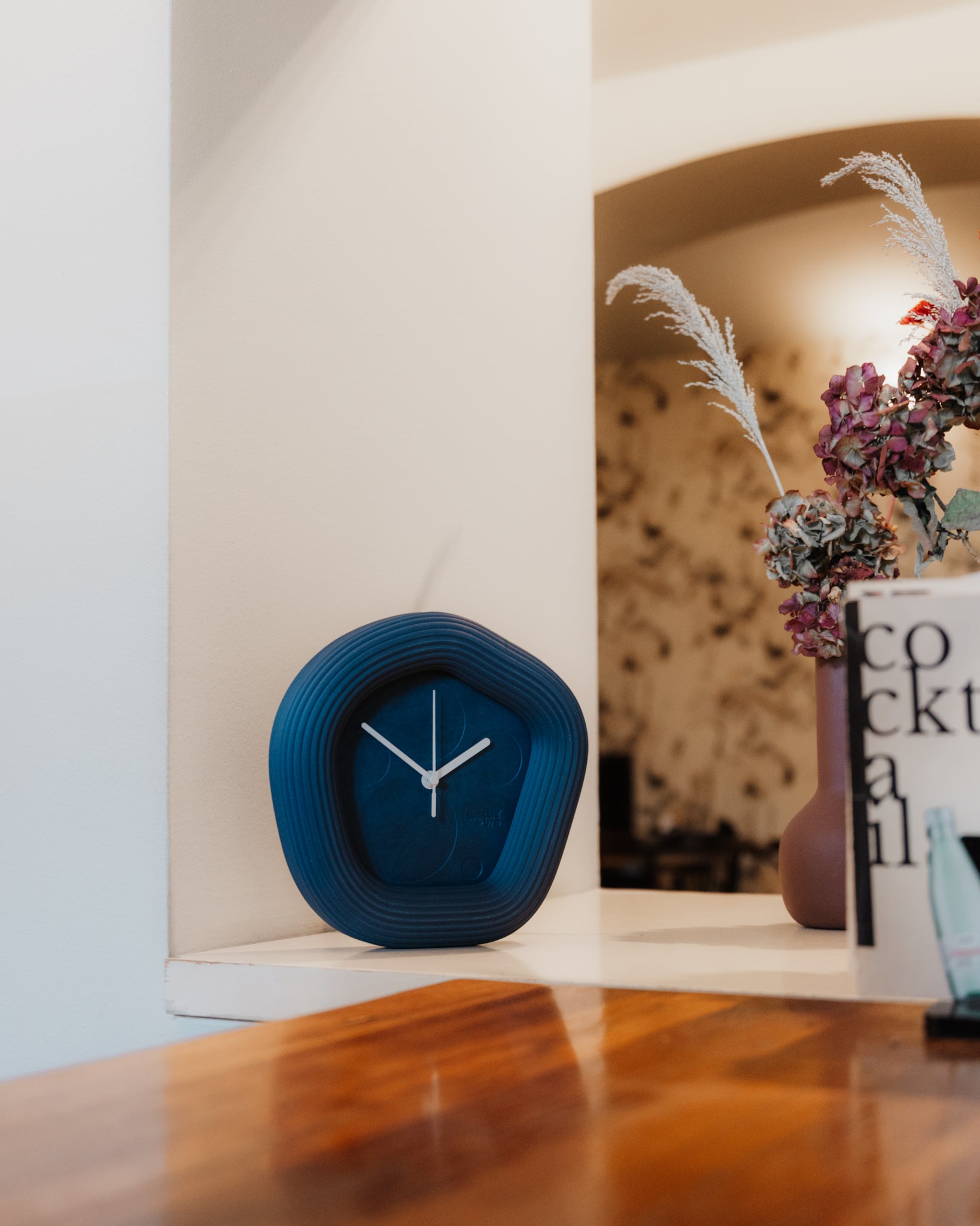 Blue clock on a wooden surface with a blurred background. Made by Ura Watches.