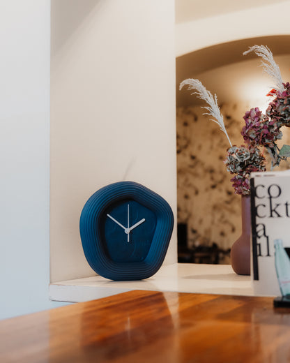 Blue clock on a wooden surface with a blurred background. Made by Ura Watches.