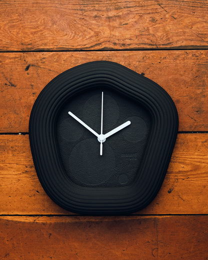 Black Wallie wall clock with white hands on a wooden surface. Made by Ura Watches / EON TIME