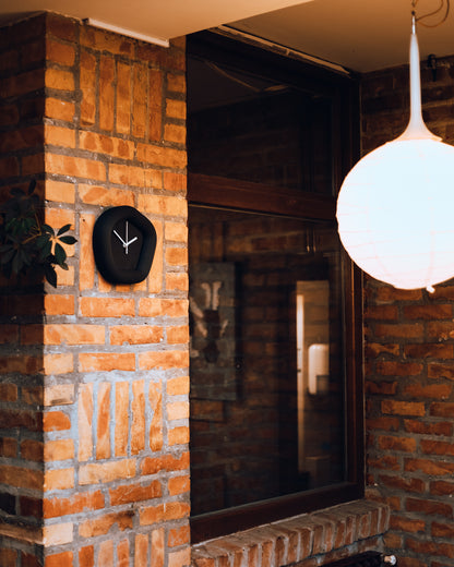 Brick wall with a Wallie clock and a hanging light fixture in a dimly lit room. Madae by Ura Watches / EON TIME