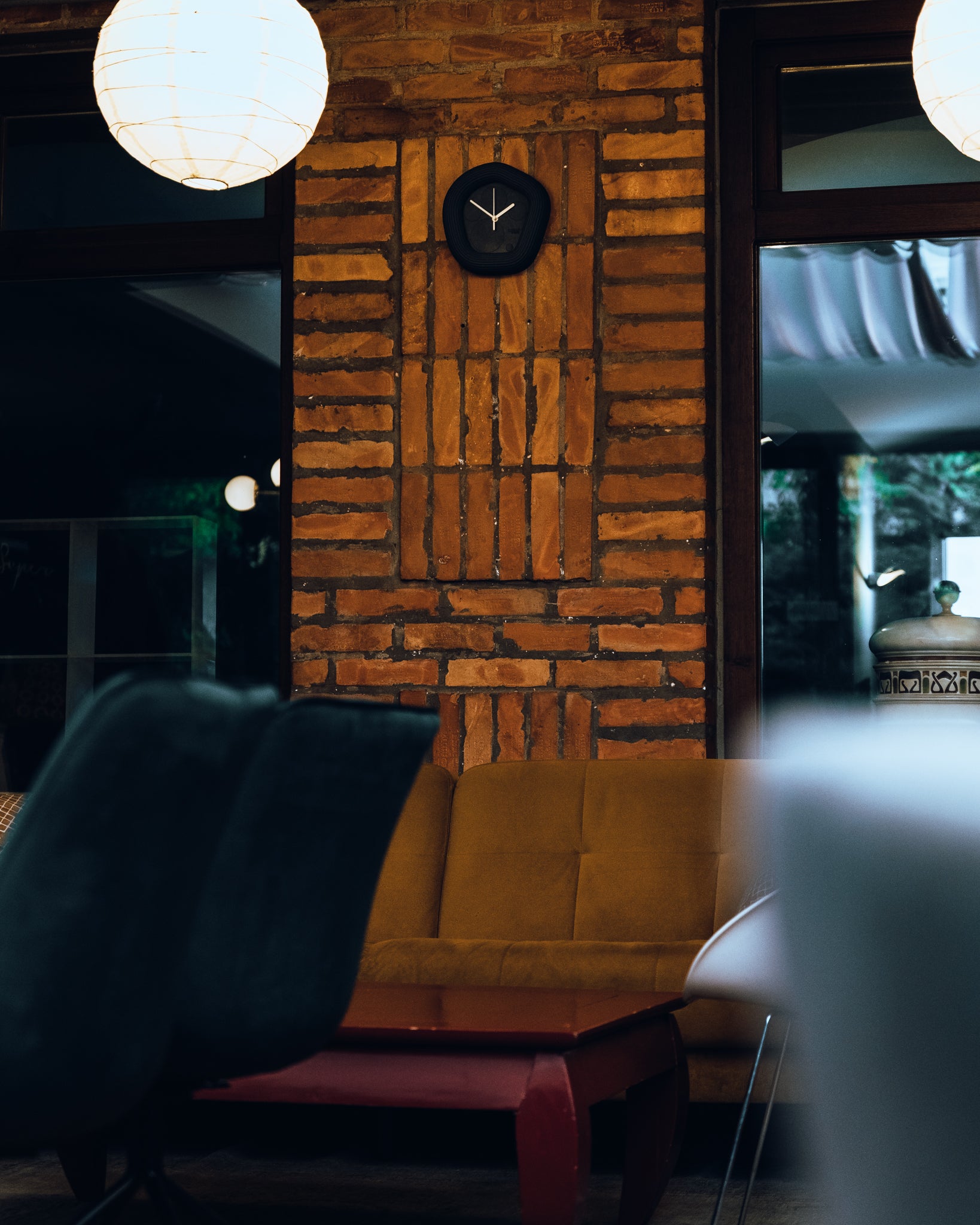Interior of a restaurant with brick wall, chairs, and a Wallie obsidian black clock. Made by Ura Watches / EON TIME