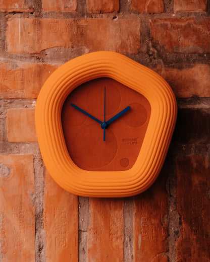 Orange Wallie wall clock with blue hands on a brick wall
