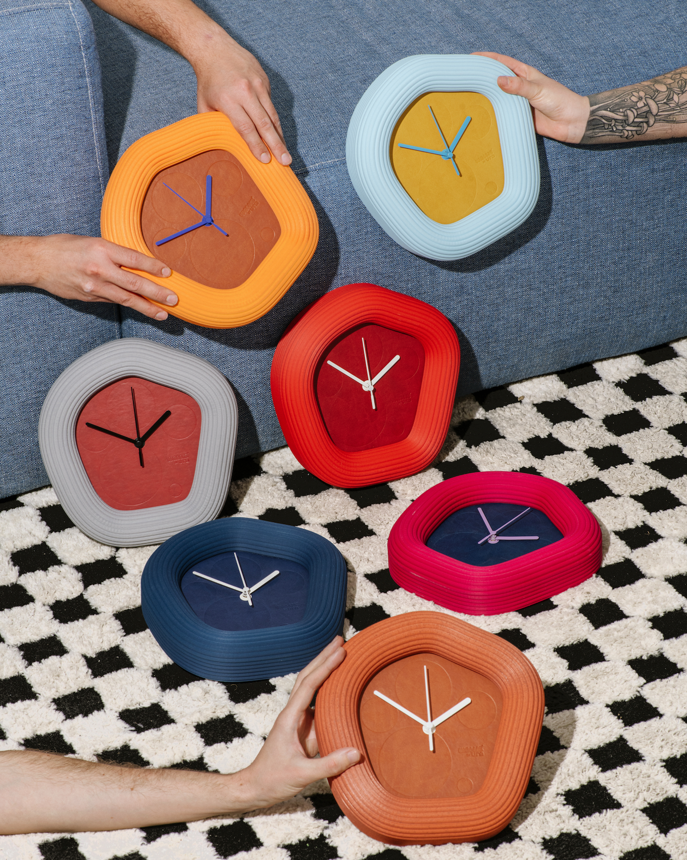 Colorful Wallie wall clocks held by people on a checkered floor. Made by Ura Watches in colaboration with Wizia studio.
